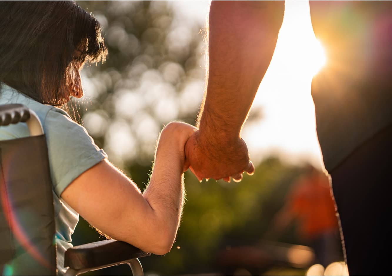 Image of girl in wheel chair holding hands with man looking at sunset